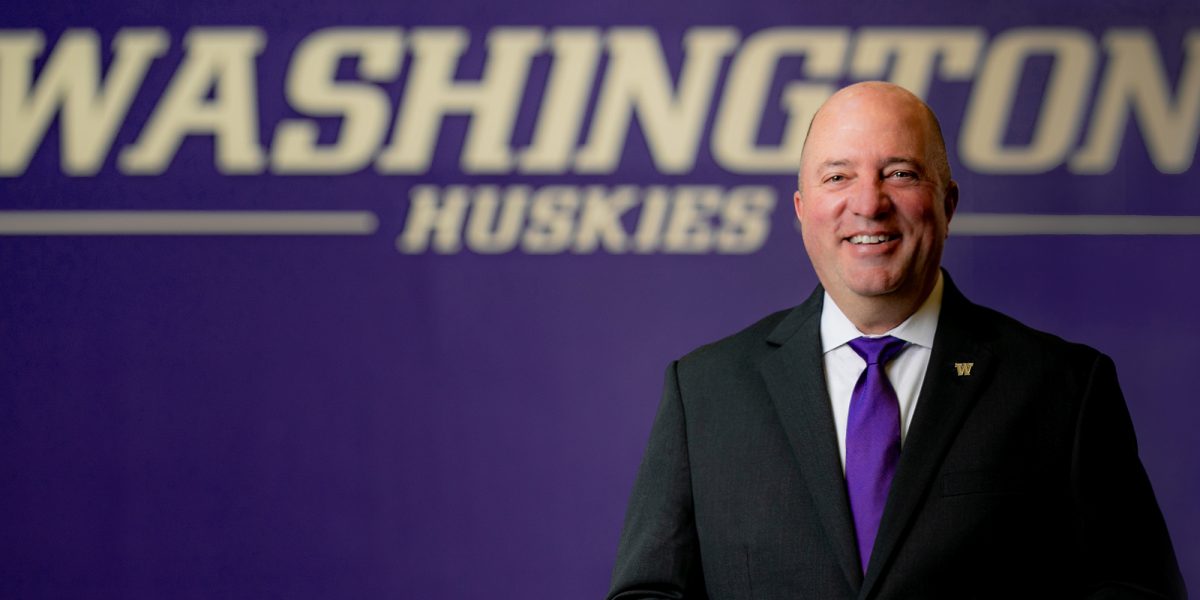 Troy Dannen stands in front of Washington Huskies gold sign against purple wall