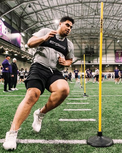 Ulumoo Ale, wearing StatSports vest, runs around agility pole in Dempsey practice facility
