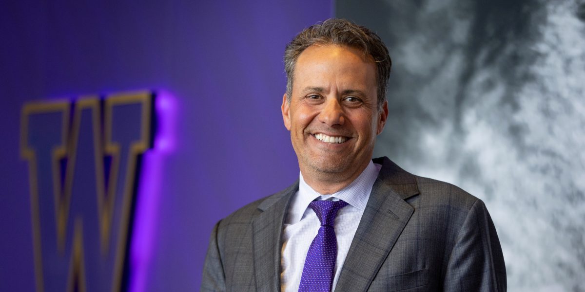 Jedd Fisch in suit standing in front of purple "W" wall