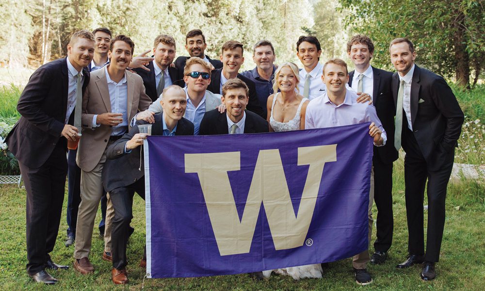 Scott and Haley Menzies, Coach Clark and 12 former Men's Soccer players pose with UW flag at wedding