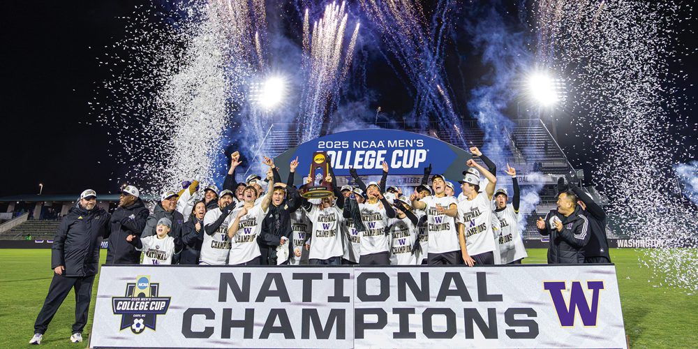 Men's Soccer team hoists trophy on field against a background of fireworks and confetti